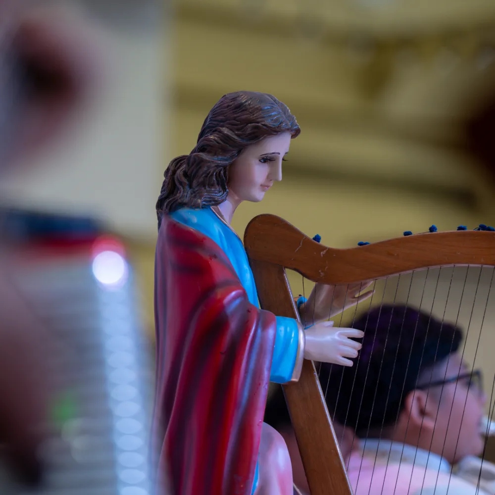 Saint Cecilia figure holding a harp in La Gran Plaza’s official festival image.