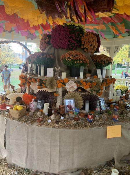 Library program photograph of the 2025 Memorial Park ofrenda with marigolds, candles, photographs and papel picado; not the 2026 installation.