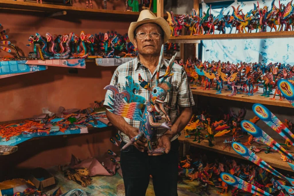 Official exhibition press photograph of an artisan among colorful folk-art sculptures; not an installation photograph from Houston.