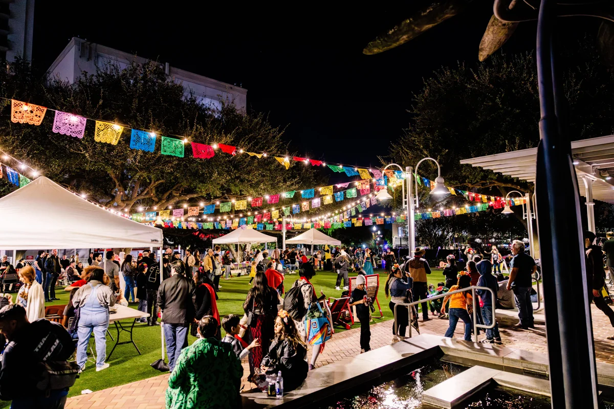 Organizer photograph of a night celebration at Market Square Park with papel picado, vendor tents and visitors.