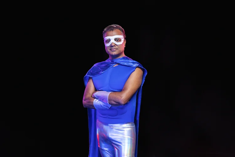 Official artist portrait of Rudresh Mahanthappa in a blue superhero costume and white eye mask, photographed by David Crow
